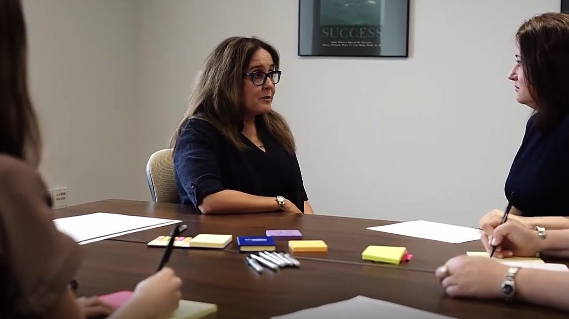 Interview methodology demonstration filmed for an instructional video, with a participant and team seated around a table